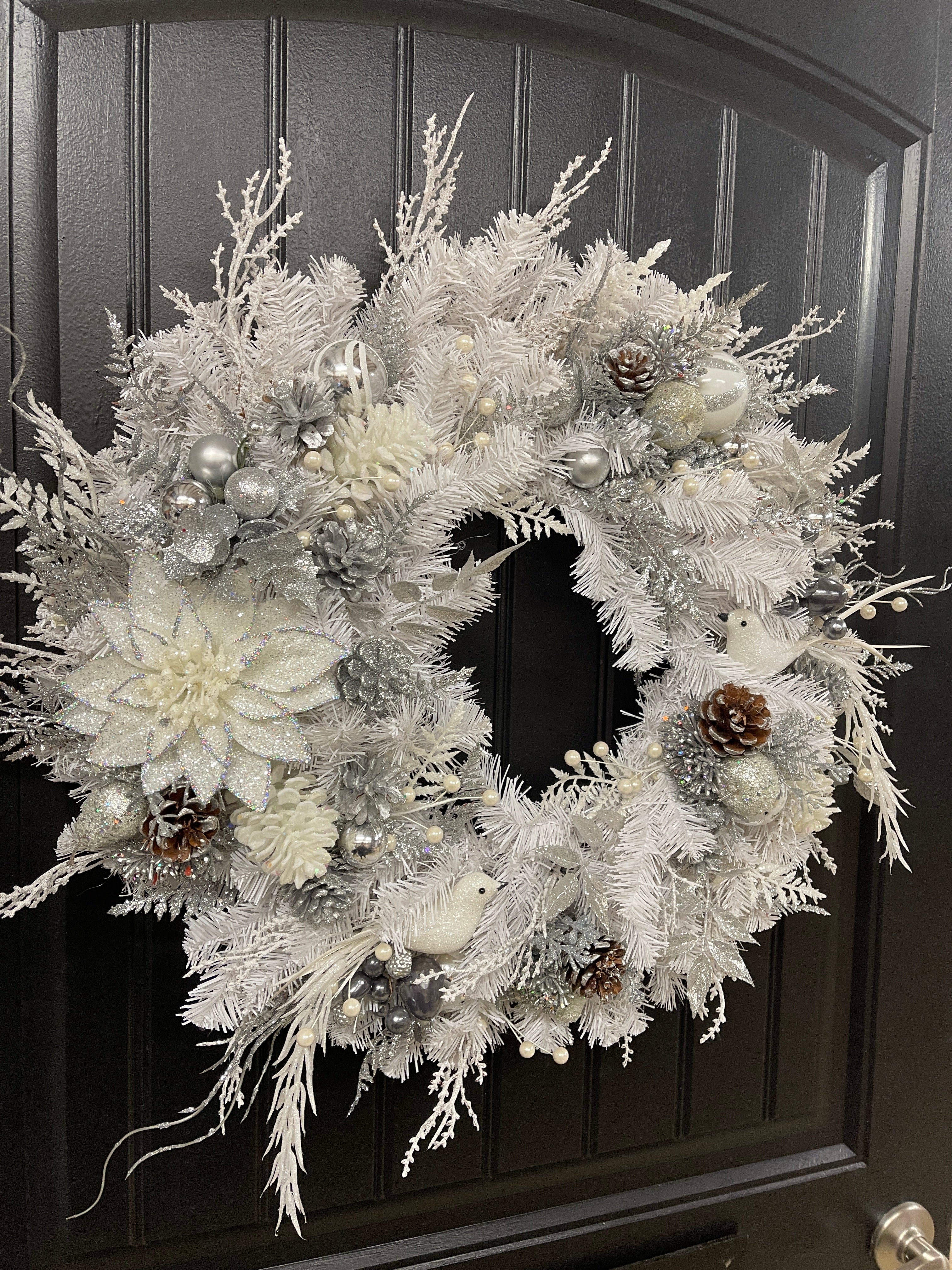Left Side View of White Evergreen Winter Wreath with White Poinsettias, Frosted Pine Cones, Christmas Balls of Silver, White and Gray, along with Silver Glittered Fern and Snow Covered Twigs and 2 White Doves on a Black Door