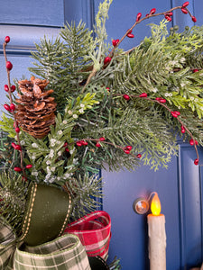 Close up of Details on a Christmas Grapevine Wreath with Artificial Pine Branches, Red Berries, Pinecones, with a Red, White and Green Bow and an Artificial Battery Operated Candle in the Center on a Blue Door