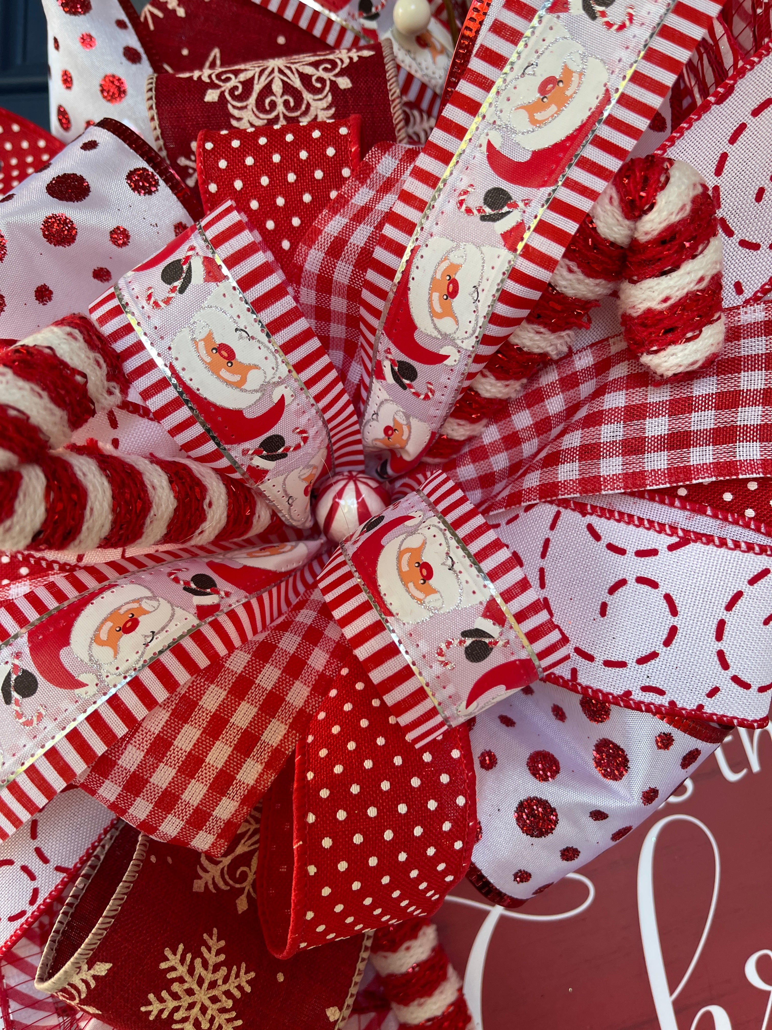 Close up of Bow featuring Santa Face Ribbon, Red and White Gingham Ribbon, Red with White Polka Dot Ribbon, Snowflakes on Red with Peppermint candy in the center