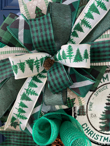 Close Up of Bow Featuring Pine Trees on White Ribbon, Black and Green Gingham Ribbon, Solid Green Ribbon, Black, White and Green Plaid Ribbon with Pine Cone in the Center