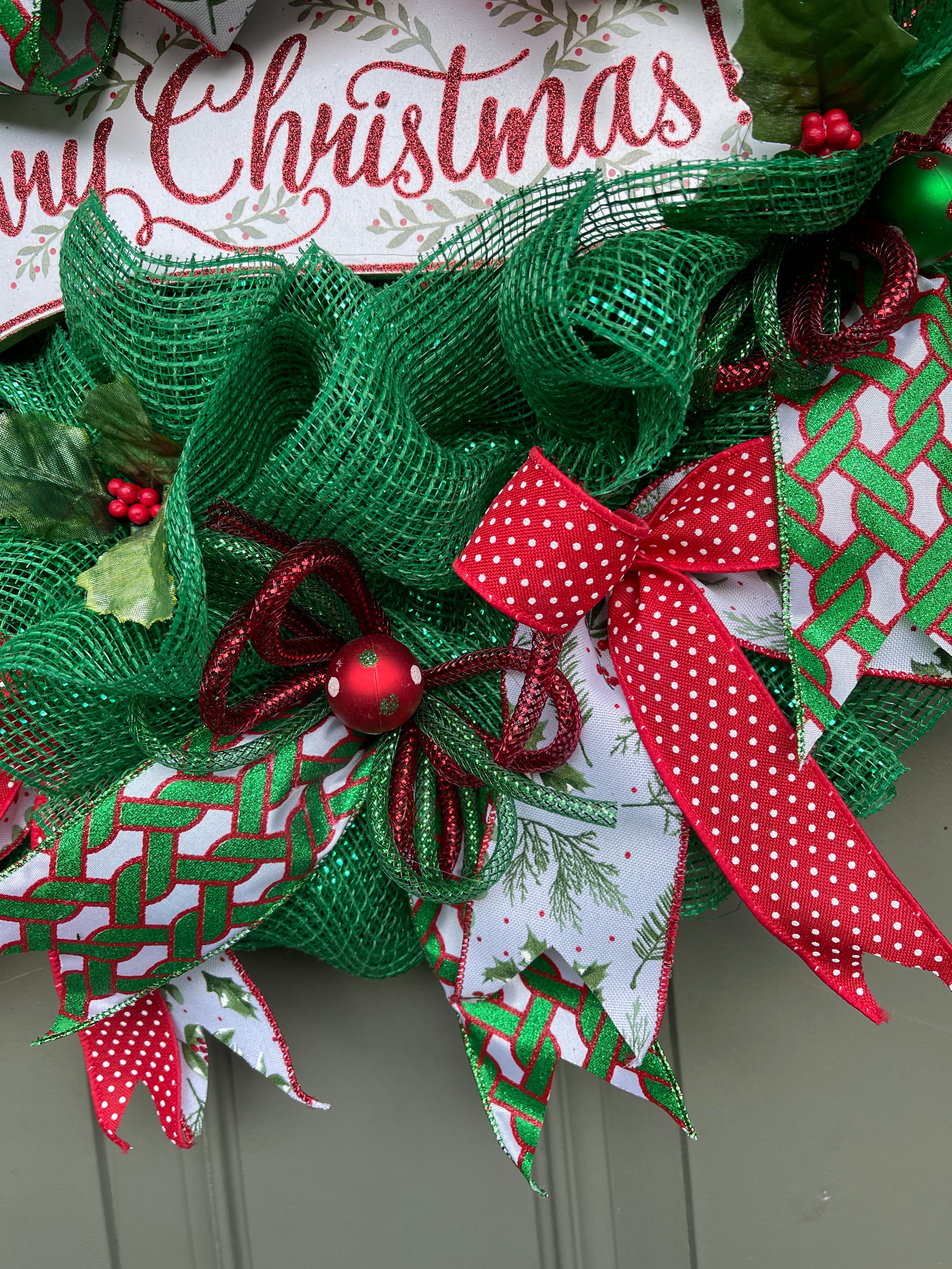 Close Up Details of Ribbons on the Edge of the Merry Christmas Wreath with Balls of White with Red and Green Polka Dots, Red Ribbon with White Polka Dots, Red and Green Flex Tubing and Mistletoe printed ribbons
